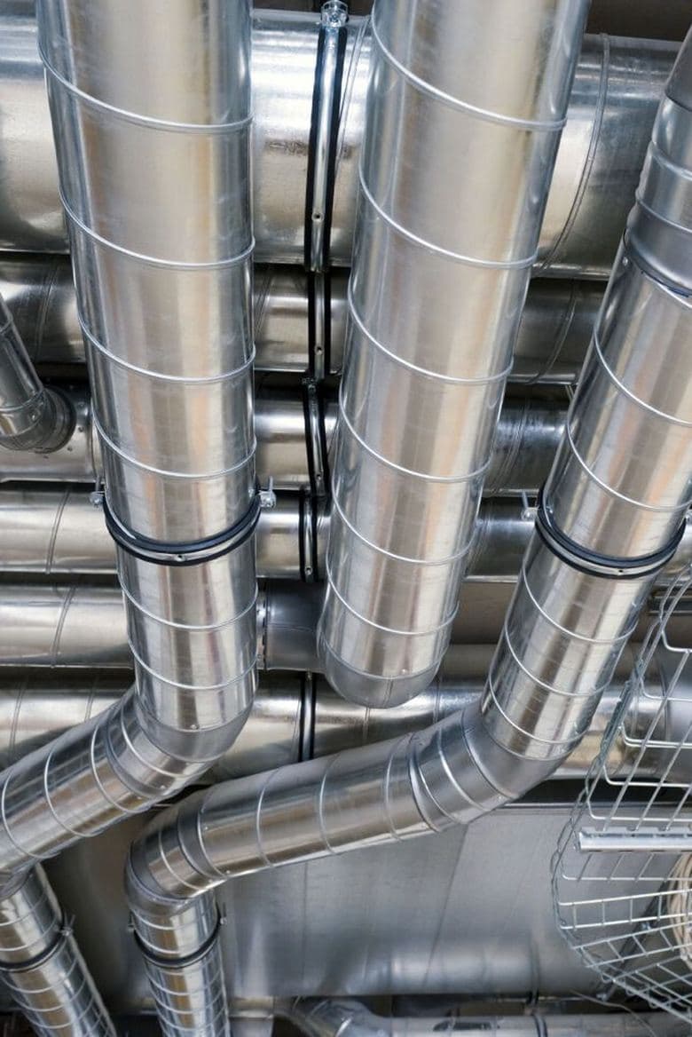 Galvaniserte ventilasjonskanaler som krysser hverandre under et tak i et teknisk rom